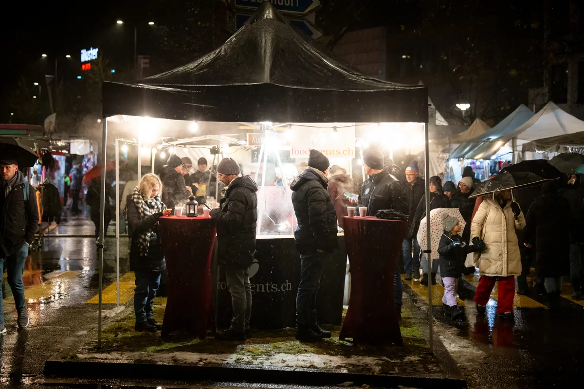 Menschen wärmen sich an einem Stand mit Glühwein.